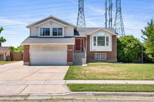 Tri-level home with an attached garage, brick siding, driveway, and roof with shingles