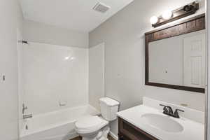 Bathroom with toilet, vanity, a textured ceiling, and  shower combination