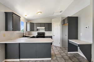Kitchen featuring black range, a sink, vaulted ceiling, a peninsula, and light countertops