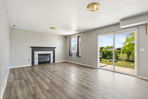 Unfurnished living room featuring a textured ceiling, wood finished floors, baseboards, and a fireplace