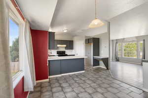 Kitchen featuring a sink, black stove, under cabinet range hood, baseboards, and a peninsula