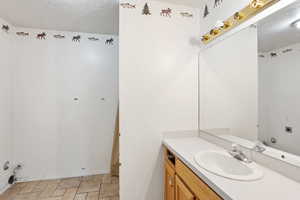 Bathroom with a textured ceiling, vanity, stone finish floors, and baseboards