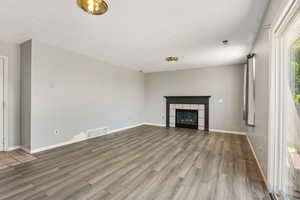 Unfurnished living room with wood finished floors, a fireplace, baseboards, and a textured ceiling