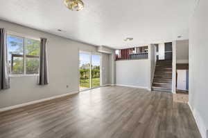 Unfurnished living room featuring wood finished floors, a textured ceiling, baseboards, and stairs