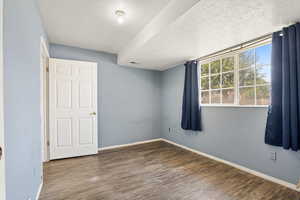Unfurnished room with a textured ceiling, wood finished floors, and baseboards