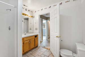 Full bath with toilet, vanity, a textured ceiling, a shower, and stone finish flooring