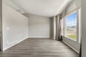 Unfurnished room with a textured ceiling, vaulted ceiling, wood finished floors, and baseboards