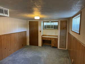 Unfurnished bedroom featuring wooden walls, a textured ceiling, carpet, a wainscoted wall, and an office area