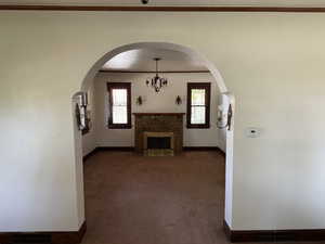 Unfurnished living room featuring baseboards, a tile fireplace, carpet, a chandelier, and ornamental molding
