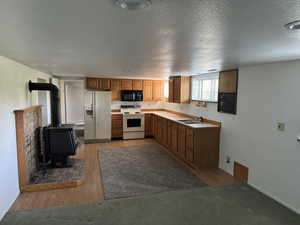 Kitchen featuring white appliances, light countertops, a wood stove, brown cabinets, and light wood-style floors
