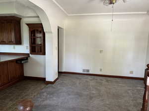 Unfurnished dining area with dark colored carpet, baseboards, and arched walkways
