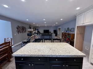 Kitchen with dark cabinetry, a center island, white cabinets, light stone counters, and recessed lighting