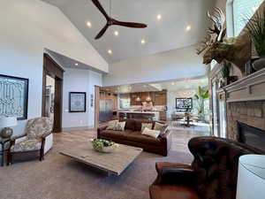 Living area with high vaulted ceiling, a ceiling fan, recessed lighting, plenty of natural light, and a stone fireplace