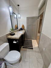 Bathroom featuring crown molding, tile patterned flooring, tile walls, toilet, and vanity