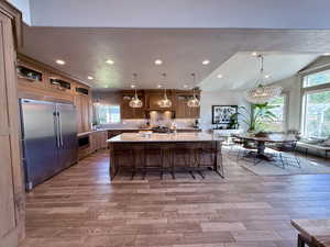Kitchen featuring stainless steel commercial refrigerator, quartz countertops, tile lwood-style floors, eat in bar area, and 10 ft center island with sink