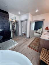 Full bathroom with a textured ceiling, a freestanding bath, a 2 shower heads, European style glass walls double vanity, and tile- wood finished floors