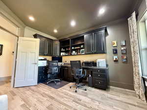 Office area with crown molding, built in study area, light wood-style flooring