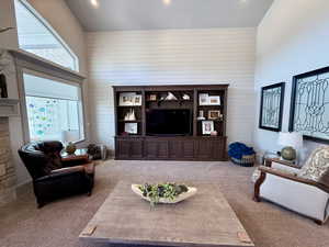 Living area with carpet, high vaulted ceiling, shiplap accent wall