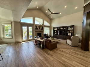 Living room with a stone fireplace, ceiling fan, high vaulted ceiling, and baseboards