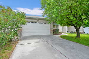 View of property hidden behind natural elements with driveway, a garage, a front lawn, and stone siding
