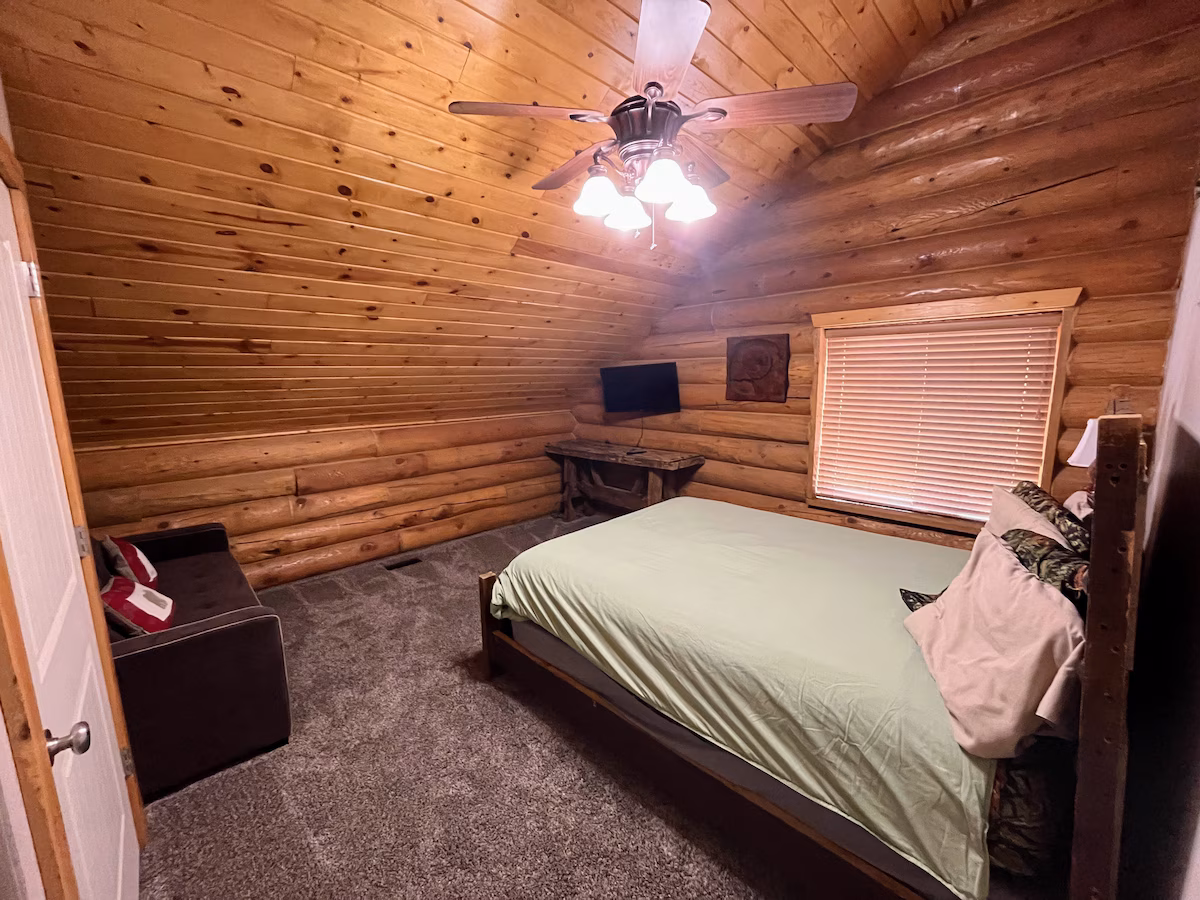 Bedroom with rustic walls, carpet, wood ceiling, vaulted ceiling, and a ceiling fan