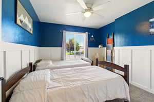 Bedroom featuring a decorative wall, carpet flooring, wainscoting, and ceiling fan