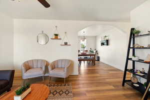 Living area with arched walkways, light wood-style flooring, baseboards, and a ceiling fan