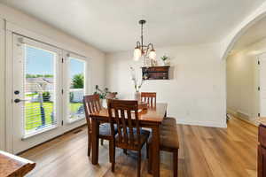 Dining room with arched walkways, light wood finished floors, baseboards, and a chandelier