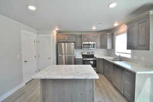 Kitchen with stainless steel appliances, a sink, light wood finished floors, a center island, and recessed lighting