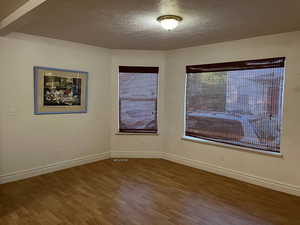 Empty room with wood finished floors, a textured ceiling, and baseboards