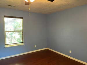 Unfurnished room featuring a textured ceiling, dark wood-style flooring, and baseboards