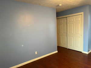 Unfurnished bedroom with baseboards, dark wood-style floors, a textured ceiling, and a closet
