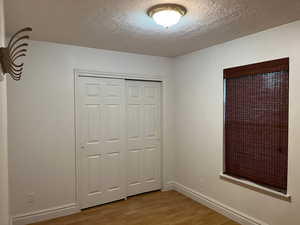 Unfurnished bedroom with wood finished floors, a textured ceiling, baseboards, and a closet
