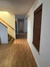 Corridor with light wood-style floors, baseboards, stairs, and a textured ceiling