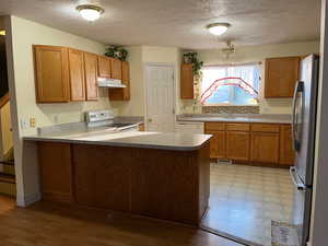 Kitchen with white appliances, a sink, a peninsula, under cabinet range hood, and a textured ceiling