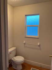 Bathroom featuring toilet, wood finished floors, baseboards, and a textured ceiling