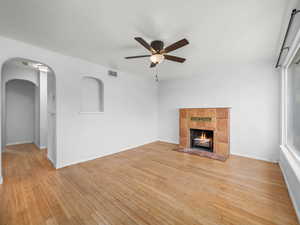 Unfurnished living room featuring ceiling fan, light wood-style floors, a fireplace, arched walkways, and baseboards