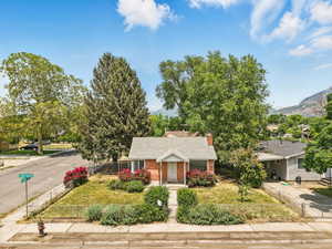 View of front of home with brick siding, concrete driveway, roof with shingles, a chimney, and a mountain view