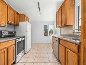 Kitchen featuring appliances with stainless steel finishes, a sink, brown cabinetry, and light tile patterned flooring