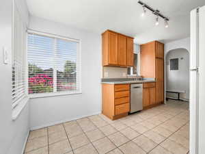 Kitchen featuring stainless steel dishwasher, electric panel, light countertops, brown cabinetry, and light tile patterned flooring