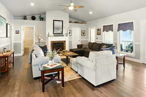 Living area featuring ceiling fan, lofted ceiling, dark wood-type flooring, a fireplace, and baseboards