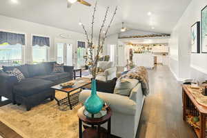 Living area with a ceiling fan, vaulted ceiling, wood finished floors, and plenty of natural light