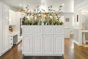 Kitchen with white cabinetry, dark wood finished floors, light countertops, stainless steel double oven, and baseboards