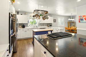 Kitchen featuring a sink, backsplash, stainless steel gas stovetop, white cabinetry, and a center island