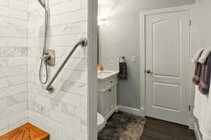 Bathroom with a tile shower, vanity, baseboards, and wood finished floors