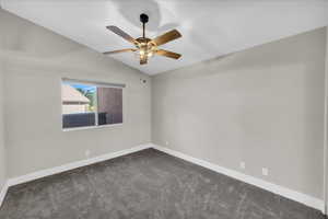 Spare room featuring a ceiling fan, vaulted ceiling, dark colored carpet, and baseboards