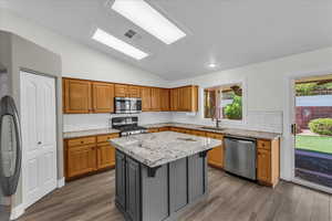 Kitchen with appliances with stainless steel finishes, a sink, lofted ceiling, a kitchen island, and wood finished floors
