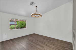 Empty room featuring a chandelier, wood finished floors, baseboards, and lofted ceiling