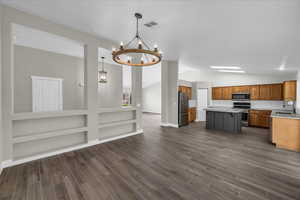Kitchen with stainless steel appliances, lofted ceiling, brown cabinets, a chandelier, and a sink