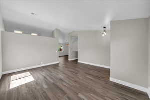 Spare room with dark wood finished floors, baseboards, and vaulted ceiling